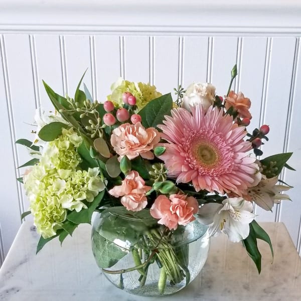 Pink gerbera and peach carnations in a round glass vase