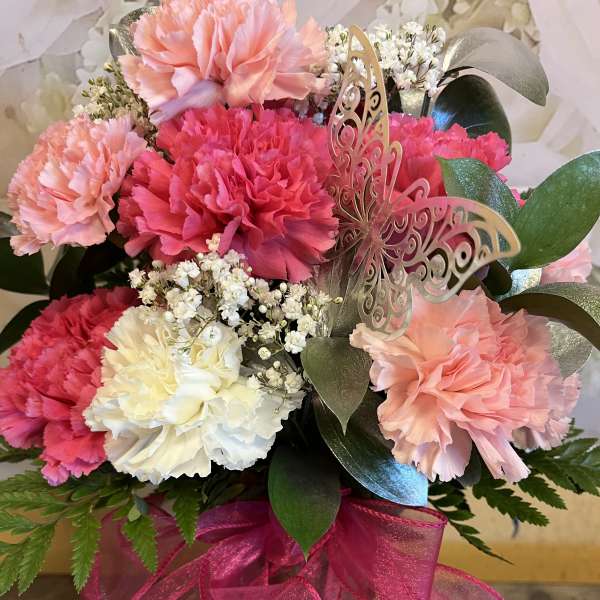 Pink and white carnations with a butterfly decoration in a glass vase