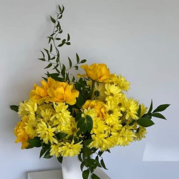 Yellow flowers arranged in a white vase with dark green foliage