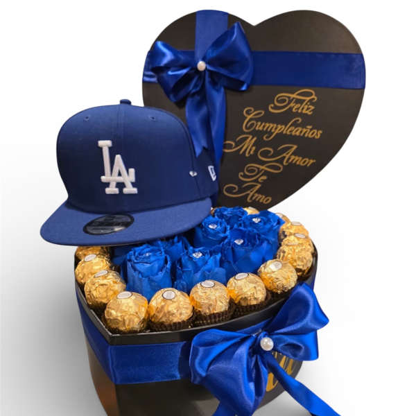 Heart-shaped gift box with blue ribbon, chocolates, and a blue LA cap