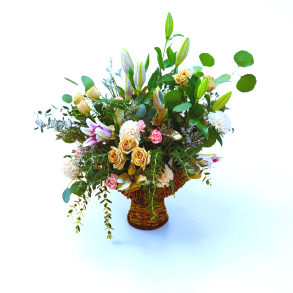 Basket arrangement of peach roses, pink lilies, and mixed blooms with tall buds.