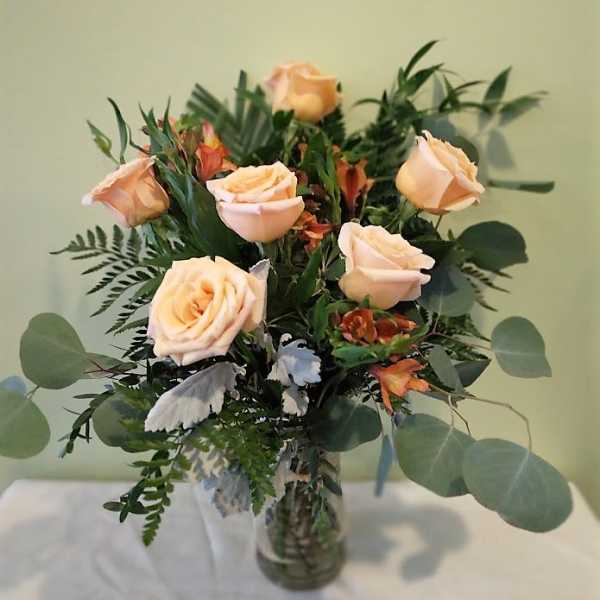 Peach roses in a glass vase with mixed greenery