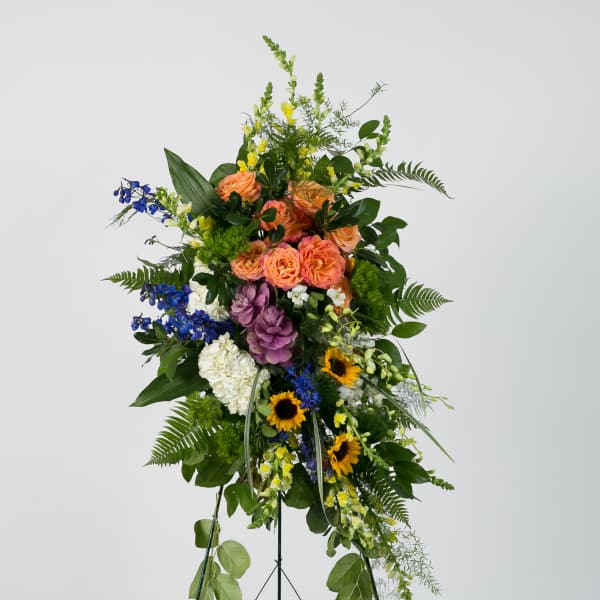 Tall standing floral spray with mixed blooms in peach, blue, yellow, white, and purple