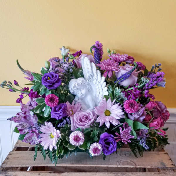 Purple and pink floral arrangement with a white angel figurine