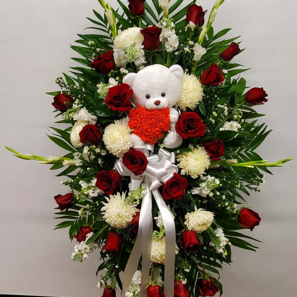 Standing floral spray with red roses, white blooms, and a teddy bear centerpiece