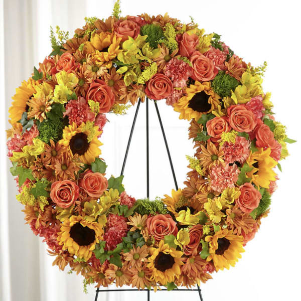 Large floral wreath with sunflowers, roses, and orange blooms on a black stand