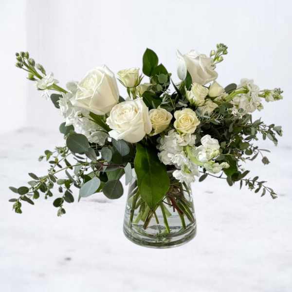 White rose and stock arrangement with foliage in a clear glass vase