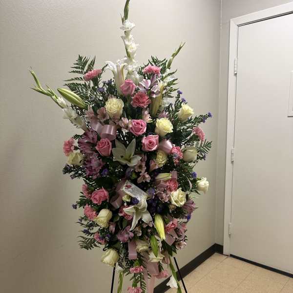 Standing spray of pink and white flowers with ribbons on a black easel in a hallway
