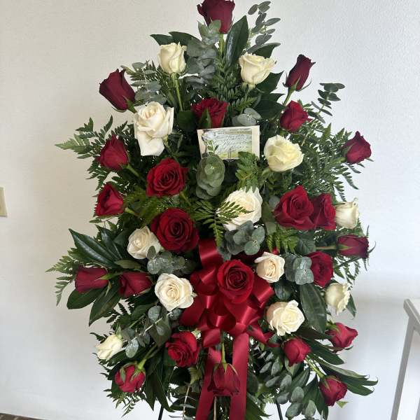 Standing spray of red and white roses with a red bow on a metal easel