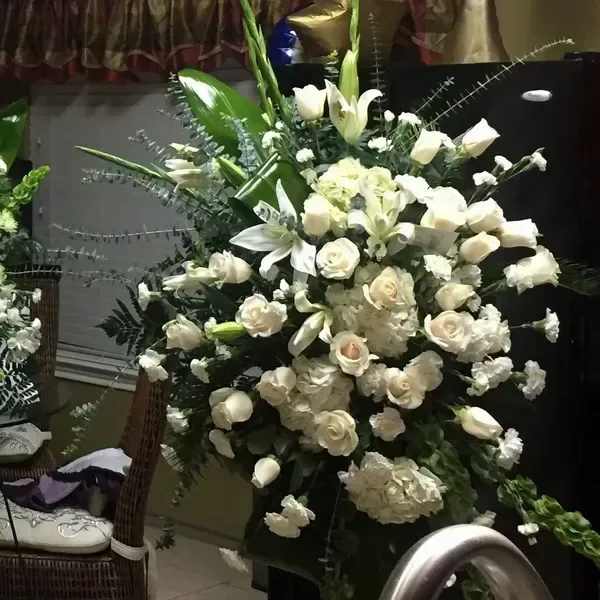 Tall white arrangement with roses, lilies, hydrangeas, and carnations in a fan-shaped design