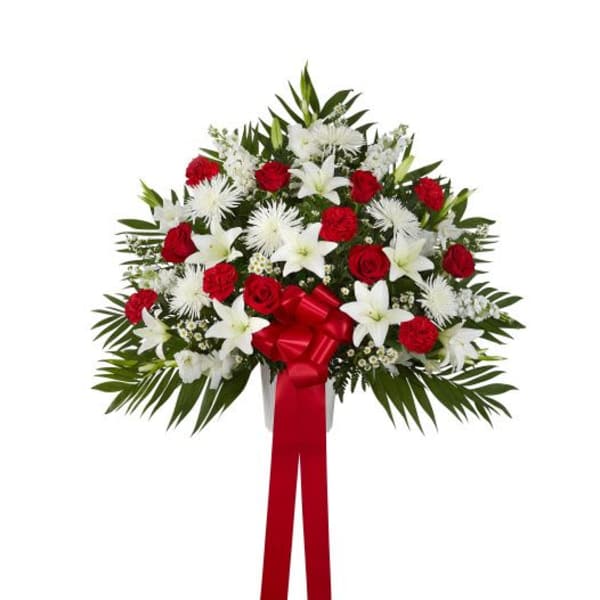 Fan-shaped standing arrangement of red roses and carnations with white lilies and mums, finished with a red bow and ribbon