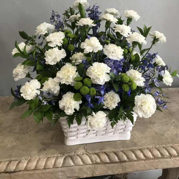 White carnations and blue flowers arranged in a white basket