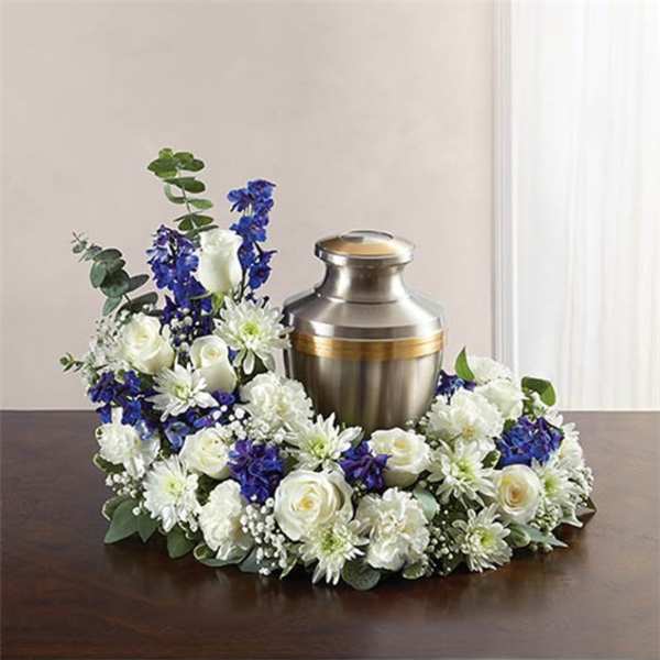 Circular white and blue floral wreath arranged around a silver cremation urn on a table