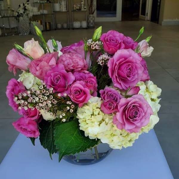 Low arrangement of pink roses and pale hydrangeas in a clear glass bowl vase