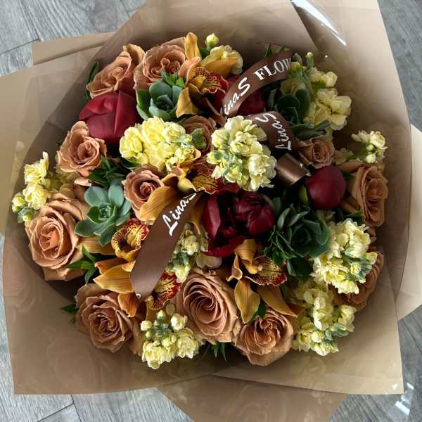Bouquet of tan roses, yellow blooms, and red flowers wrapped in brown paper