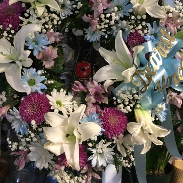 Floral wreath with white lilies, purple and blue daisies, and a blue ribbon
