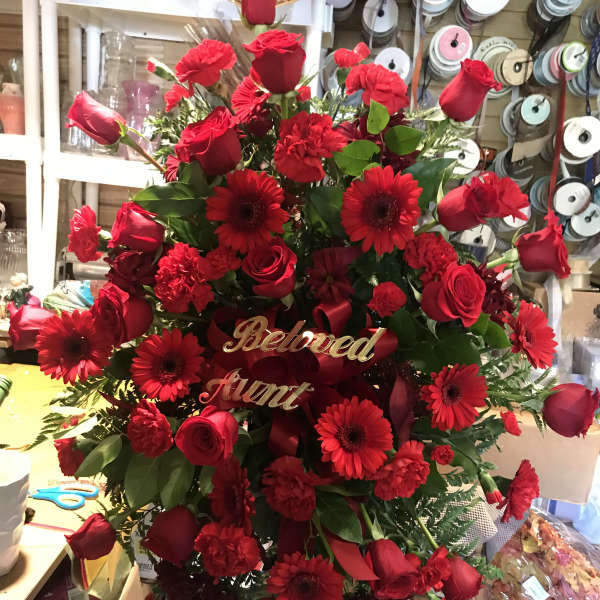 Red roses and gerbera daisies arranged in a standing spray with a "Beloved Aunt" sign.