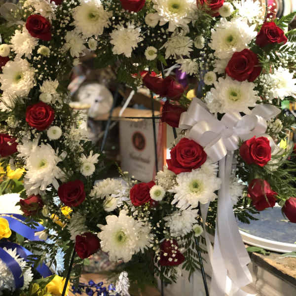 Heart-shaped wreath of red roses and white daisies with a white ribbon