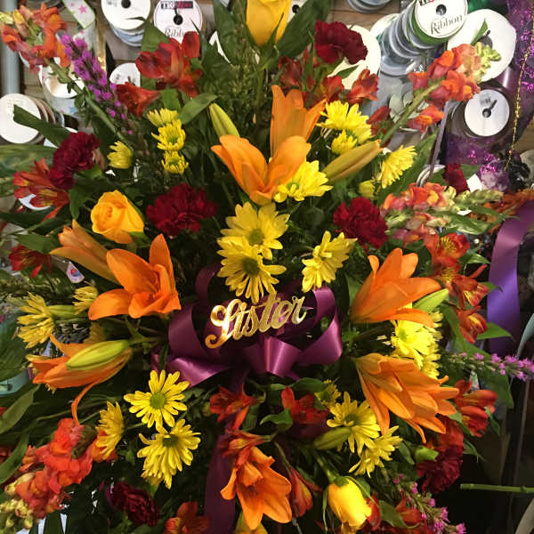 Large mixed bouquet with orange lilies, yellow daisies, and red flowers tied with a purple ribbon