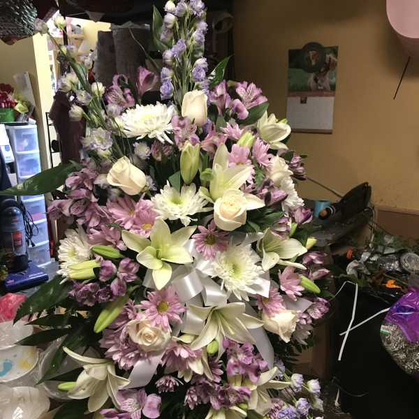 Large pastel floral spray with lilies, roses, daisies, and purple filler flowers