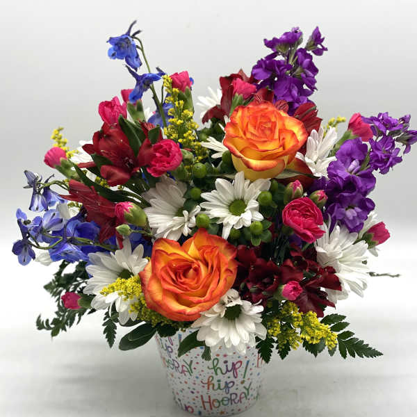 Colorful mixed bouquet in a patterned cup with orange roses and daisies