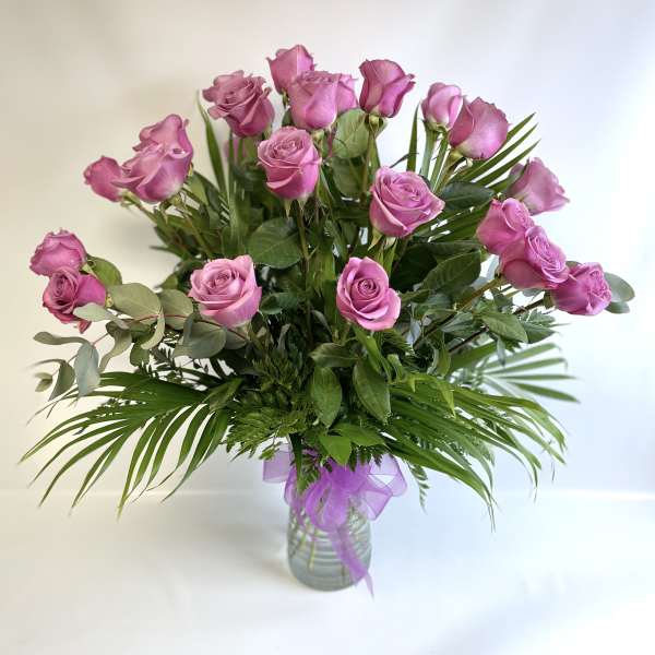 Pink roses in a glass vase with a purple ribbon