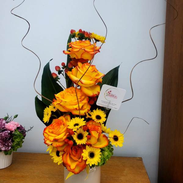 Tall arrangement of orange roses and yellow daisies in a white vase