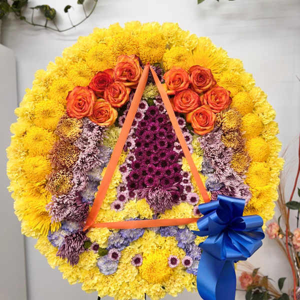 Large floral wreath with yellow, orange, and purple flowers and a blue ribbon