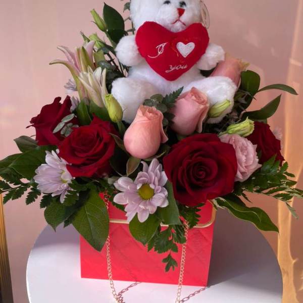 Red roses and pink flowers arranged with a teddy bear and "I LOVE YOU" topper