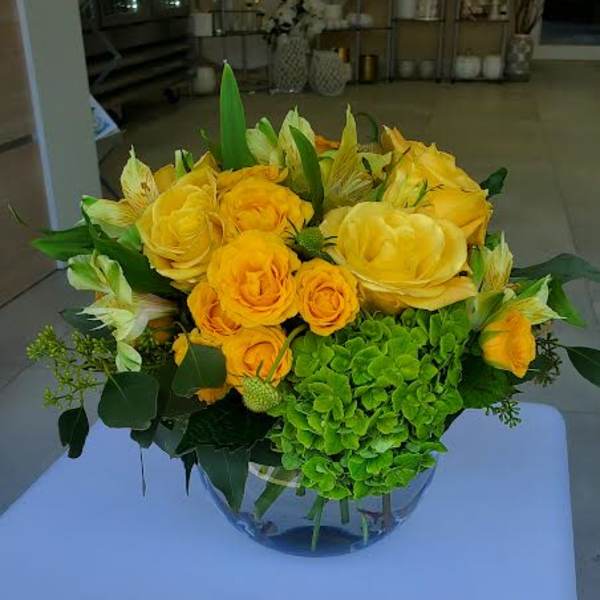 Low arrangement of yellow roses and alstroemeria with green hydrangea in a clear glass bowl vase