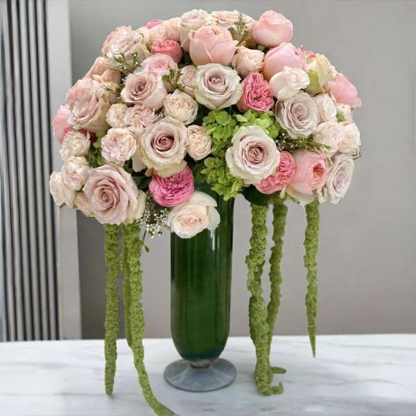 Pink and white rose arrangement in a green glass vase with trailing green accents