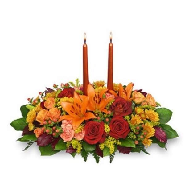 Low centerpiece of orange lilies, red and peach roses with two tall orange taper candles
