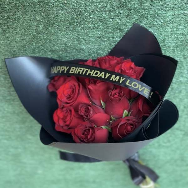 Bouquet of red roses wrapped in black paper with a birthday ribbon