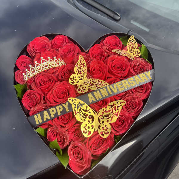 Heart-shaped box of red roses with anniversary ribbon and butterfly decorations