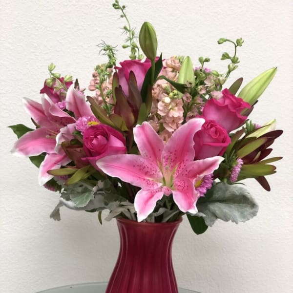 Pink lilies and roses arranged in a red glass vase
