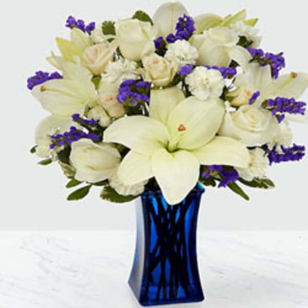 White lilies and roses with purple accents in a blue vase