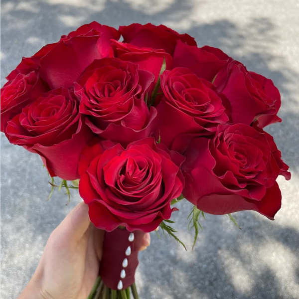 Handheld bouquet of red roses with a burgundy ribbon wrap
