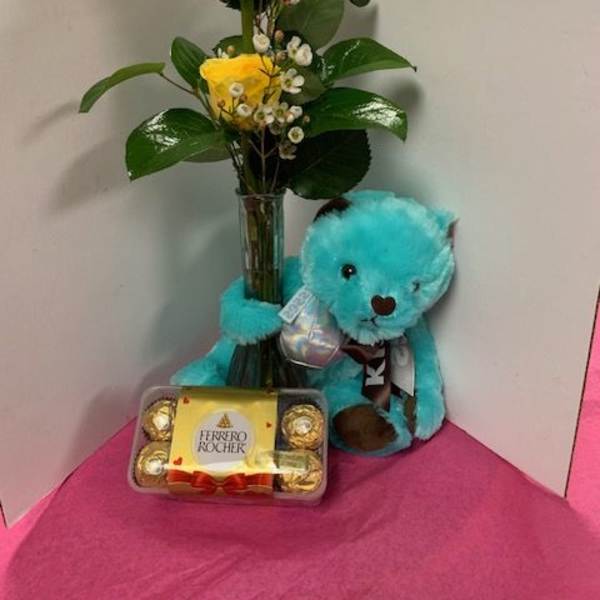 Yellow roses in a glass vase with a blue teddy bear and chocolates