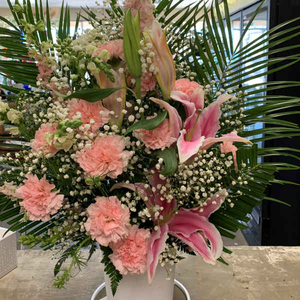 Tall pink floral arrangement in a white container with palm fronds