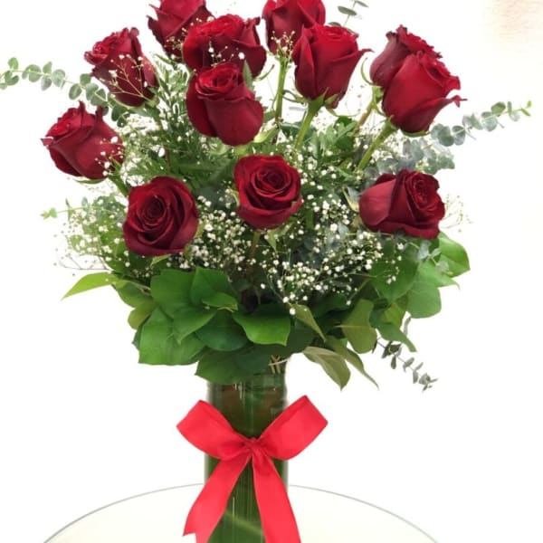 Red roses arranged in a glass vase with a red ribbon