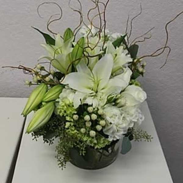 White lily arrangement in a round container with curly branches