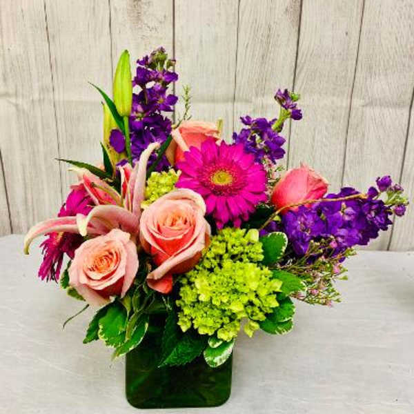 Mixed bouquet of pink roses, purple blooms, and green hydrangea in a glass vase