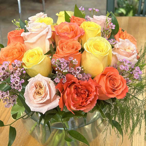 Mixed roses in orange, yellow, and blush arranged in a glass vase