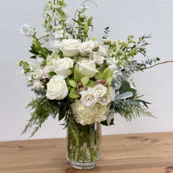 White floral arrangement in a clear glass vase with mixed blooms and greenery