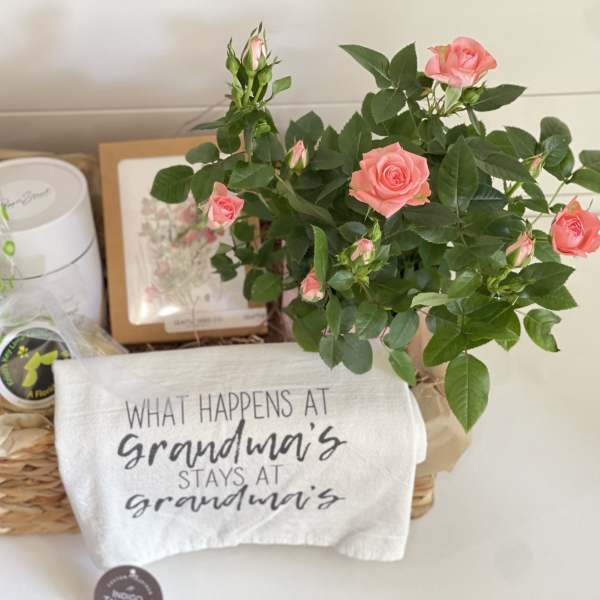 Pink rose plant in a basket with a printed towel and gift items