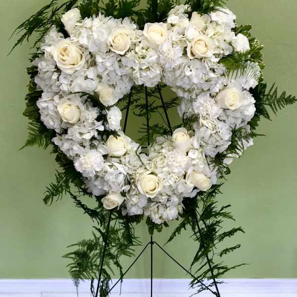 Heart-shaped white floral wreath on a stand with trailing greenery