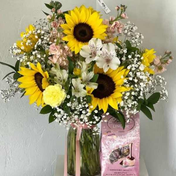 Bouquet of sunflowers and white flowers in a glass vase with a pink gift box
