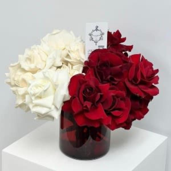 Red and white rose arrangement in a dark glass vase