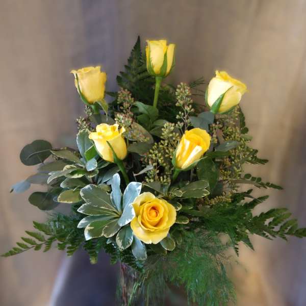 Yellow roses arranged in a glass vase with mixed greenery