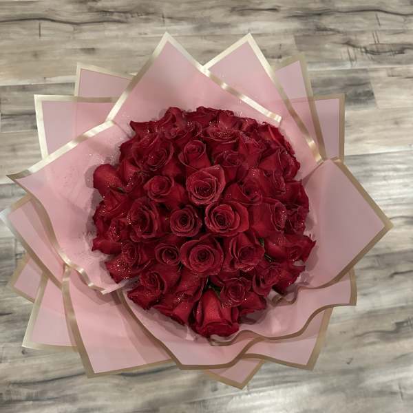 A bouquet of red roses wrapped in pink paper with gold trim.